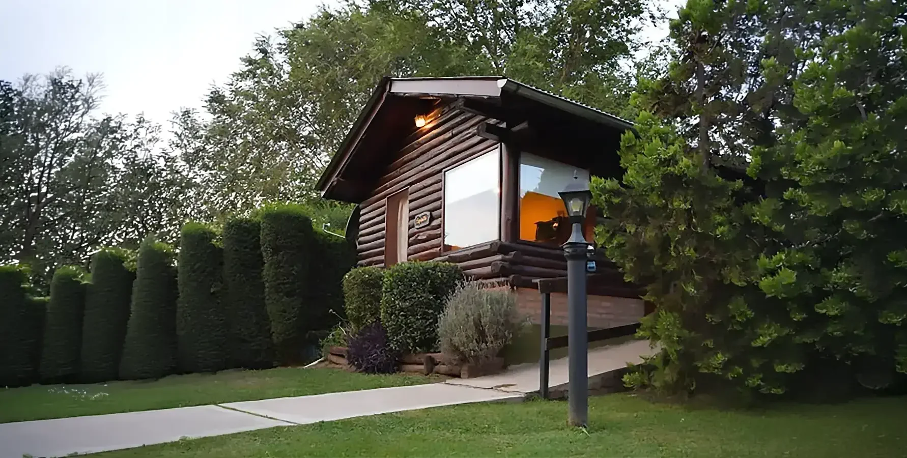 Exterior de cabaña de madera en entorno natural con jardín y vegetación.
